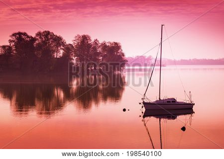 Little sailing boat reflects in the serene water during sunrise. Masuria Poland.