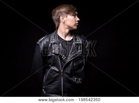 Troubled teenager in leather jacket turned away on black background