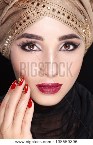 Gorgeous Young East Woman face portrait in hijab. Beauty Model Girl with bright eyebrows, perfect make-up, touching her face. Traditional. Isolated on black background. Smokey.Jewelry on her face