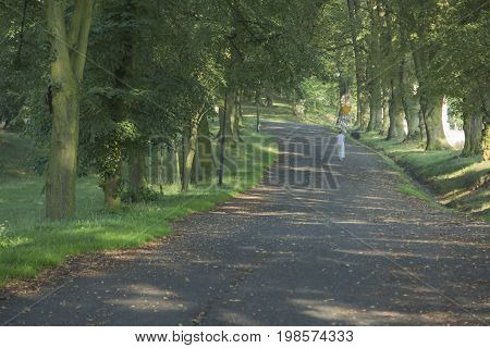 A woman walks a linden alley on a summer morning