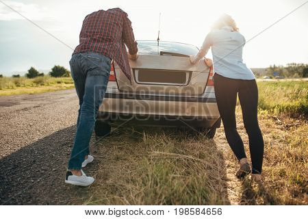 Man and woman pushing a broken car, back view