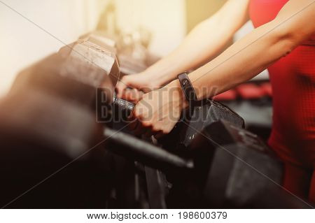 girl takes a hand dumbbells, on her arm is wearing a fitness bracelet, a smart watch in the gym. Blick light, light.