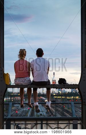 Young couple in love on romantic date sitting on railway bridge with a bottle of wine and watching the sunset over Munich urban city center. Just the two of us.