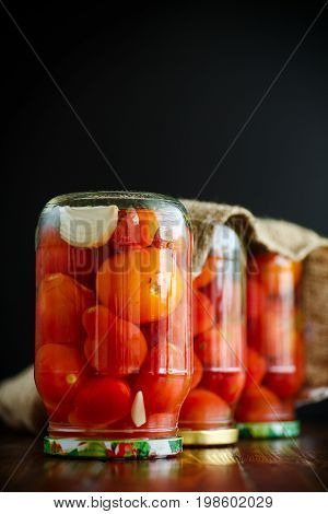 Home preservation. Canned in a glass jar ripe tomatoes on a wooden table.