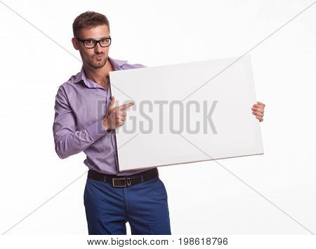 Young jocular man portrait of a confident businessman showing presentation, pointing paper placard gray background. Ideal for banners, registration forms, presentation, landings, presenting concept.
