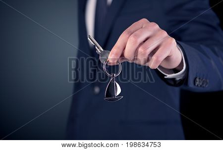Young businessman hand over keys with empty dark background