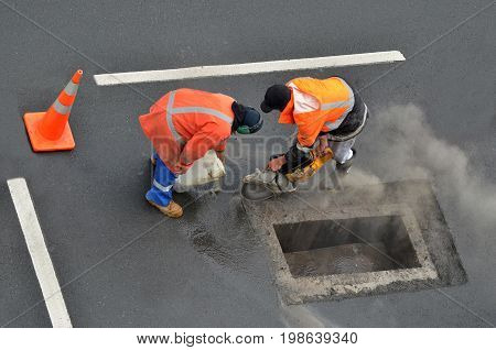 Aerial view of unrecognizable road workers cutting asphalt or concrete with saw blade at construction site