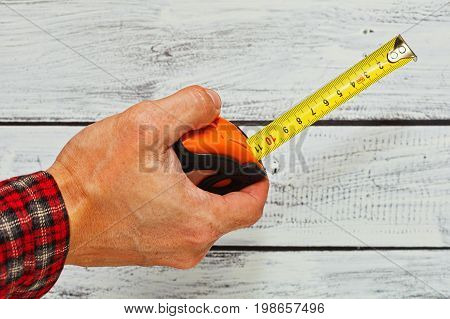 Male hand in checkered work shirt holding a tape-measure - construction or engineering concept