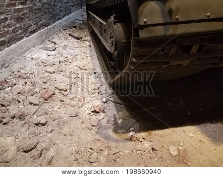 treads of old green tank on ground near red brick wall