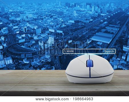 Search www button with wireless computer mouse on wooden table over city tower street and expressway Searching system and internet concept