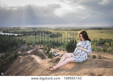 Happy beautiful pregnant girl puts her hands on her belly