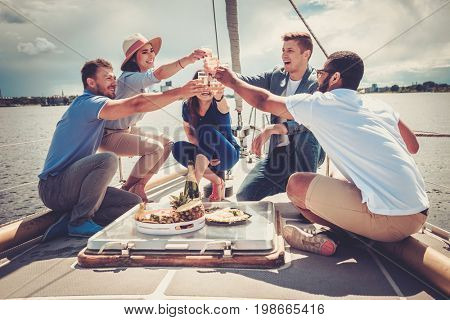 Happy friends eating fruits and drinking on a yacht
