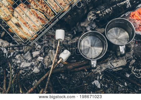 top view on bonfire with chicken meat and cup with water and murshmallows