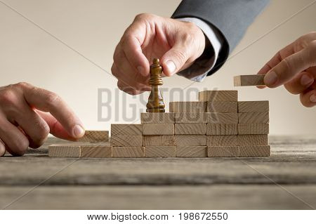 Business success and promotion concept with a businessman moving a chess piece up a series of steps formed by building blocks being put in place by his team in a close up view.