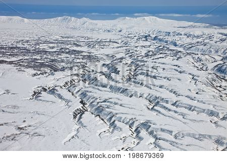 Mountainous terrain ravines erosion of the surface around the volcano on the Kamchatka Peninsula. Neighborhood Karymsky volcano after a fresh snowfall in the spring from a helicopter. Russia.