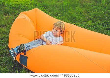 Cute Boy Resting On An Air Sofa In The Park.