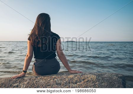 woman sits on the rock and lookin for lake on sunset