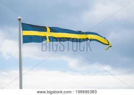 Swedish pennant flag on a flagpole in the wind in blue and yellow colors in cloudy weather