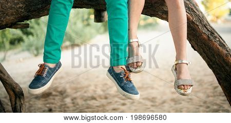 Little girl and boy sit side by side on tree branch. First love. Only their legs are visible.