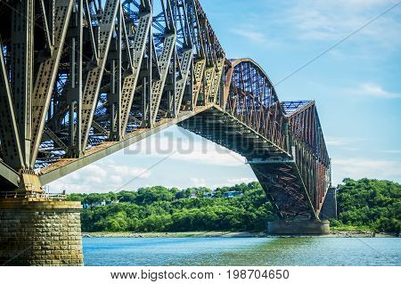 Beautiful old metal city bridge spanning a large river seen from below with blue sky overhead history and landscape