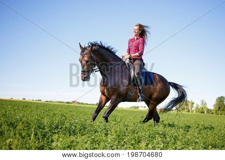 Happy young woman galloping horseback on field and enjoying feeling of freedom