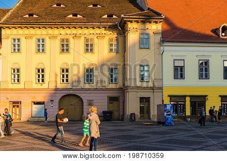 SIBIU ROMANIA - JUNE 19 2017: Large main square Huet roof with eyes in ancient house and tourists on the street at golden sun light.