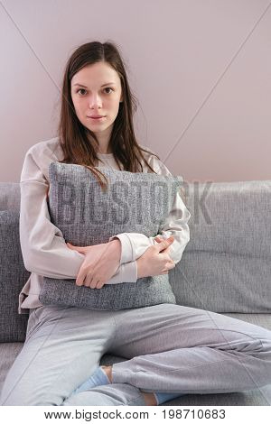 Lonely depressed woman at home, she is sitting on the sofa and hugging a pillow