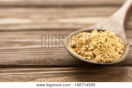 Ginger powder in wooden spoon on wooden table. Close-up.