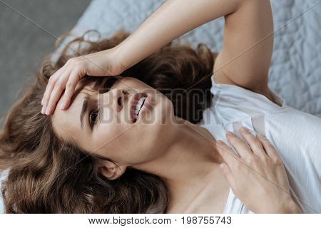 I need medicine. Cheerless unhappy moody woman holding her forehead and suffering from a headache while being at home
