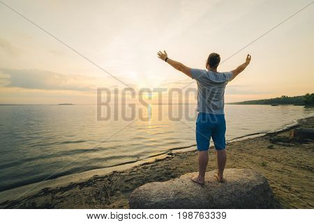 man on sand beach looking on sunrise with hands up