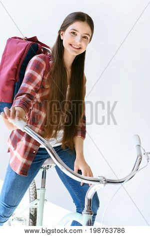 Portrait Of Smiling Teenage Girl With Backpack Sitting On Bicycle Isolated On White