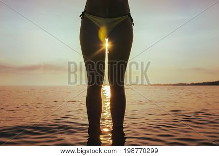 sunrise between woman legs in sweemsuite on the beach