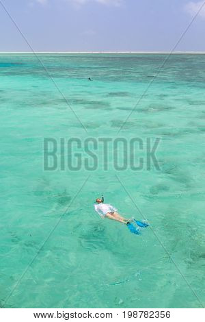 Woman snorkeling in clear shallow sea of tropical lagoon with turquoise blue water and coral reef, near exotic island. Mnemba island, Zanzibar, Tanzania.