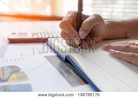 Businessman writing on notebook on wooden table People are recording accounting data calculated from calculator. To report information to the CEO. Concept finance planing and analyzes management.