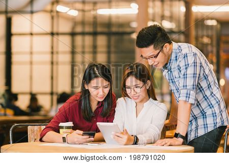 Young Asian college students or coworkers using digital tablet and smartphone together at coffee shop diverse group. Casual business freelance work at cafe social meeting or education concept