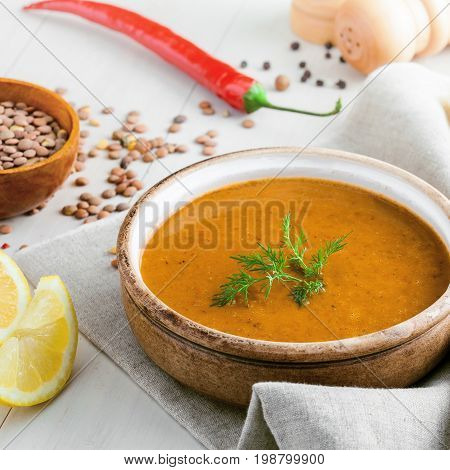 Healthy vegetarian lentil soup in a rustic clay bowl piece of bread and lemon slices on a white wooden table. Delicious healthy meal served on a canvas tablecloth.