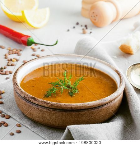 Bowl of delicious lentil soup with bread lemon slice and spoon on a white wooden table. Traditional healthy vegetarian food.