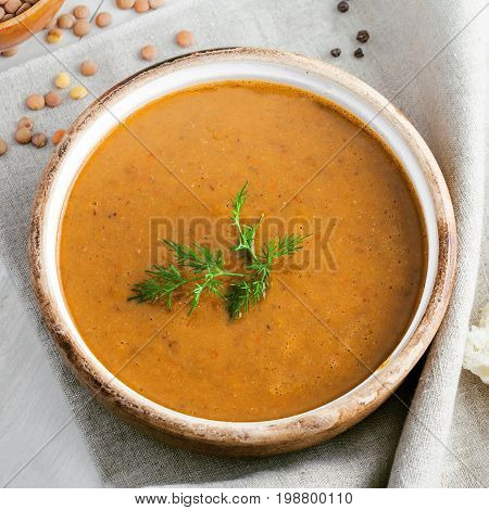Soup made of lentil and vegetables in a rustic bowl on a canvas tablecloth. Delicious healthy vegetarian food on a white wooden table. Top view.