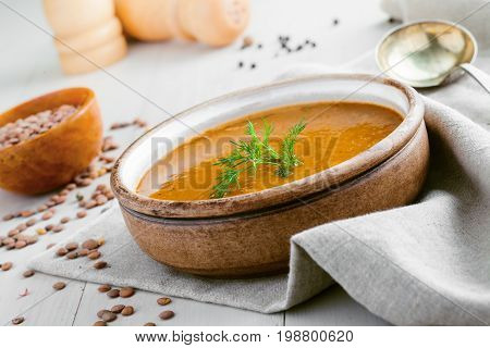Delicious soup made of lentils in a rustic clay bowl served on a canvas tablecloth. Healthy vegetarian meal on a table. Close-up shot.