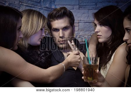 a pretty young man is surrounded by several women trying to seduce him.