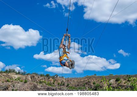 Ukraine Migea - July 30 2017: Zipline. A view of a man sliding on a steel cable against a beautiful blue sky with white clouds. Extreme and active rest.