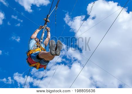 Ukraine Migea - July 30 2017: Zipline. A view of a man sliding on a steel cable against a beautiful blue sky with white clouds. Extreme and active rest.