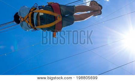Zipline. A view of a man sliding on a steel cable against a beautiful blue sky with white clouds. Extreme and active rest.