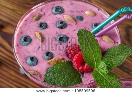 Close-up picture of a margarita glass full of refreshing and healthy smoothie on a wooden background. An organic cocktail with sweet raspeberries, blueberries and green mint. Healthful lifestyle.