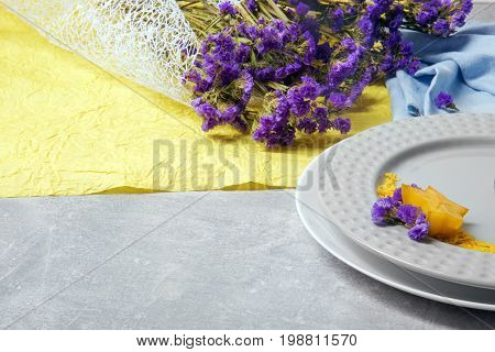 A colorful floral composition. A bouquet of little purple flowers on a blue and yellow fabric. Fancy plates on a gray table background. Health, relaxation and romance concept.