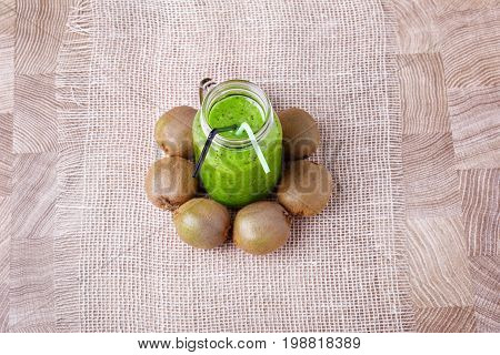 A view from above of a fresh homemade smoothie with ripe kiwi on a white tablecloth and on a light wooden background. Healthy and organic green beverage. Whole kiwis near the drink.