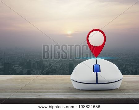Map pin location button with wireless computer mouse on wooden table over modern city tower at sunset vintage style Map pointer navigation concept
