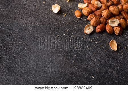 A view from above on salty appetizer for beer on a saturated black stone background. Small heap of nutritious roasted crispy hazelnuts. Peeled brown nuts. Copy space.