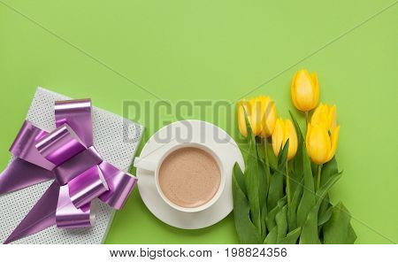 From above shot of yellow tulips on green table with giftbox and cup of coffee.
