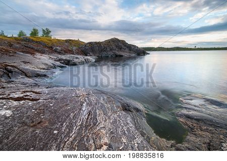 Tranquil stony coast of lake landscape under cloudy morning sky with clouds in twilight in early morning